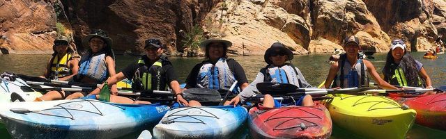 Kayakers lined on water under rock face
