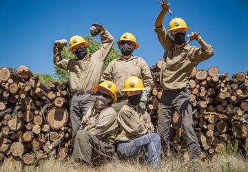 5 Crew members posing in front of logs