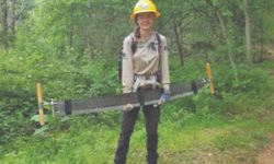 Crew member holds tool in front of a forest