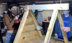 Woman uses screwdriver to construct top frame of doghouse