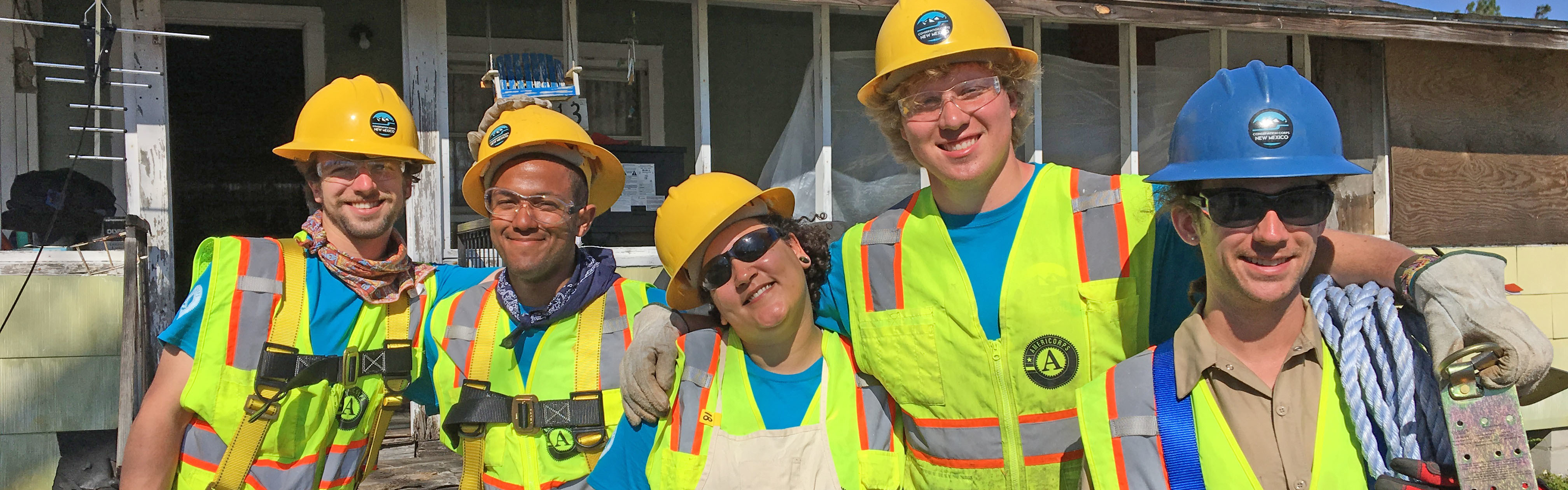 5 crew members smiling in front of building